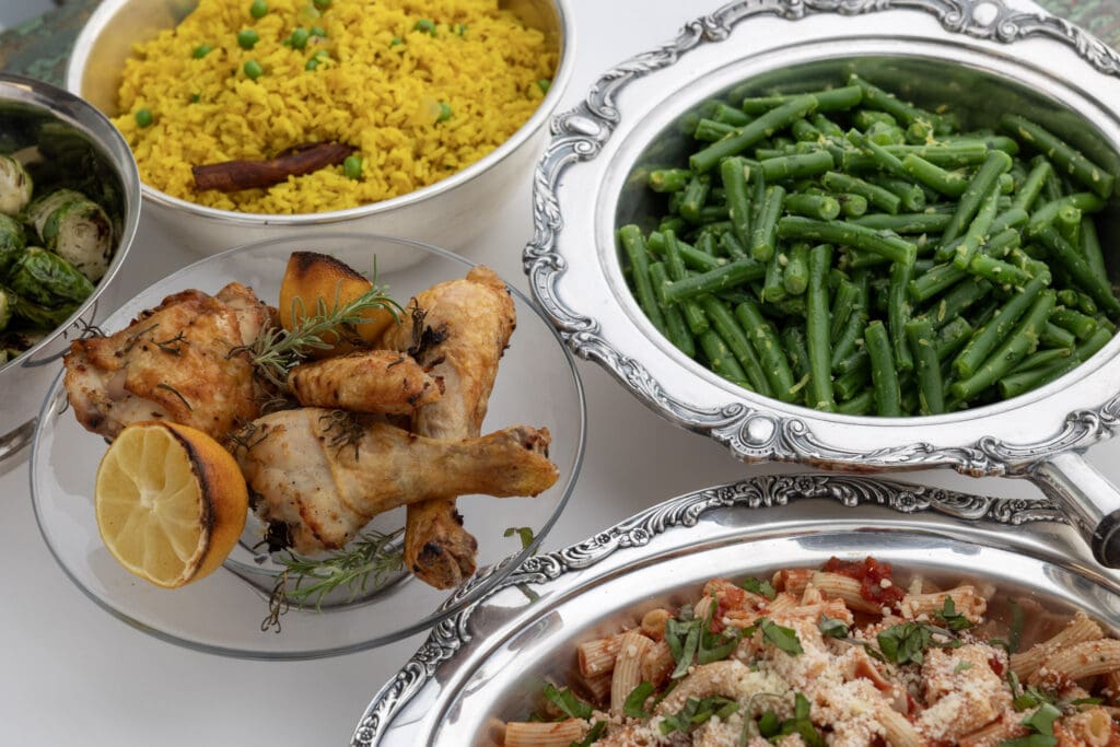 Overhead view of several food dishes in bowls: Brussels sprouts, yellow rice, chicken, green beans, pasta