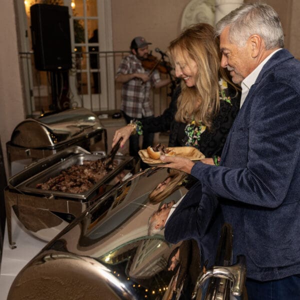 Guests serving themselves pulled pork sliders in front a buffet at a party.