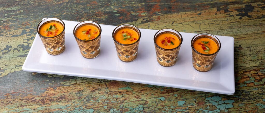 Small shot glasses with an orange soup with cucumber and red pepper garnishes