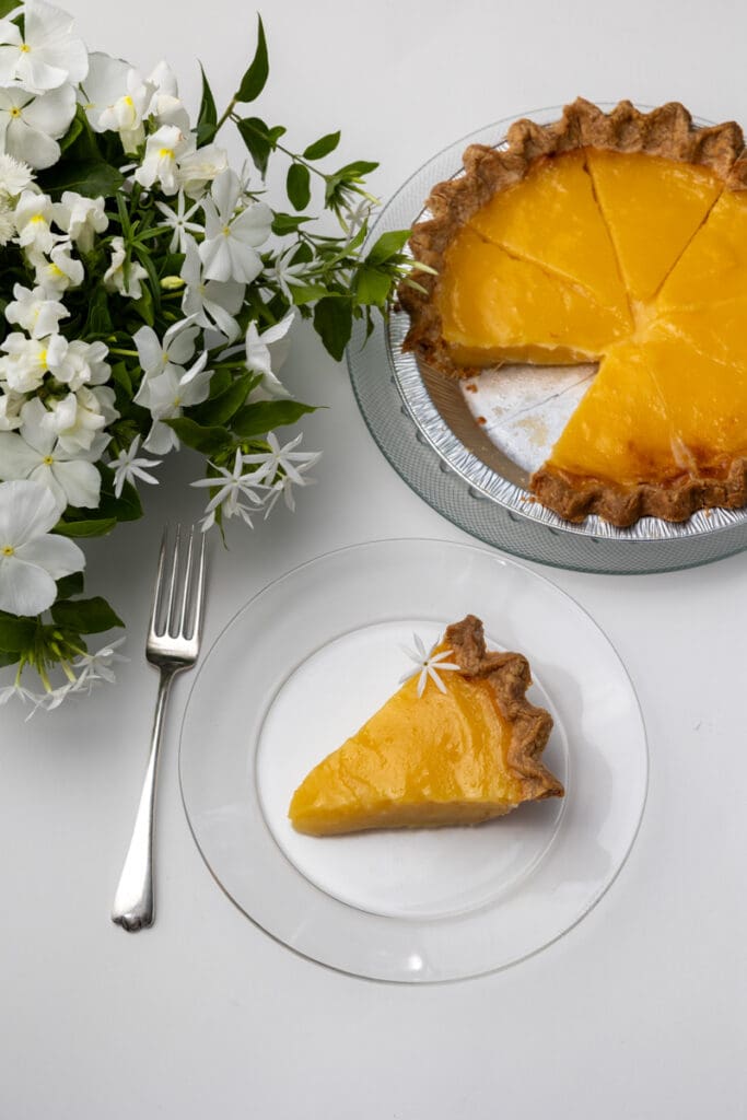 Cut lemon pie with one slice on a plate next to a vase of flowers