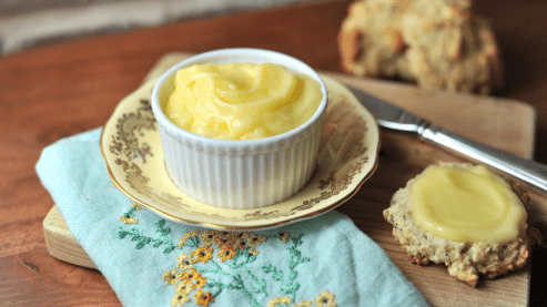 A small saucer with custard next to a scone and a piece of scone with custard already on it