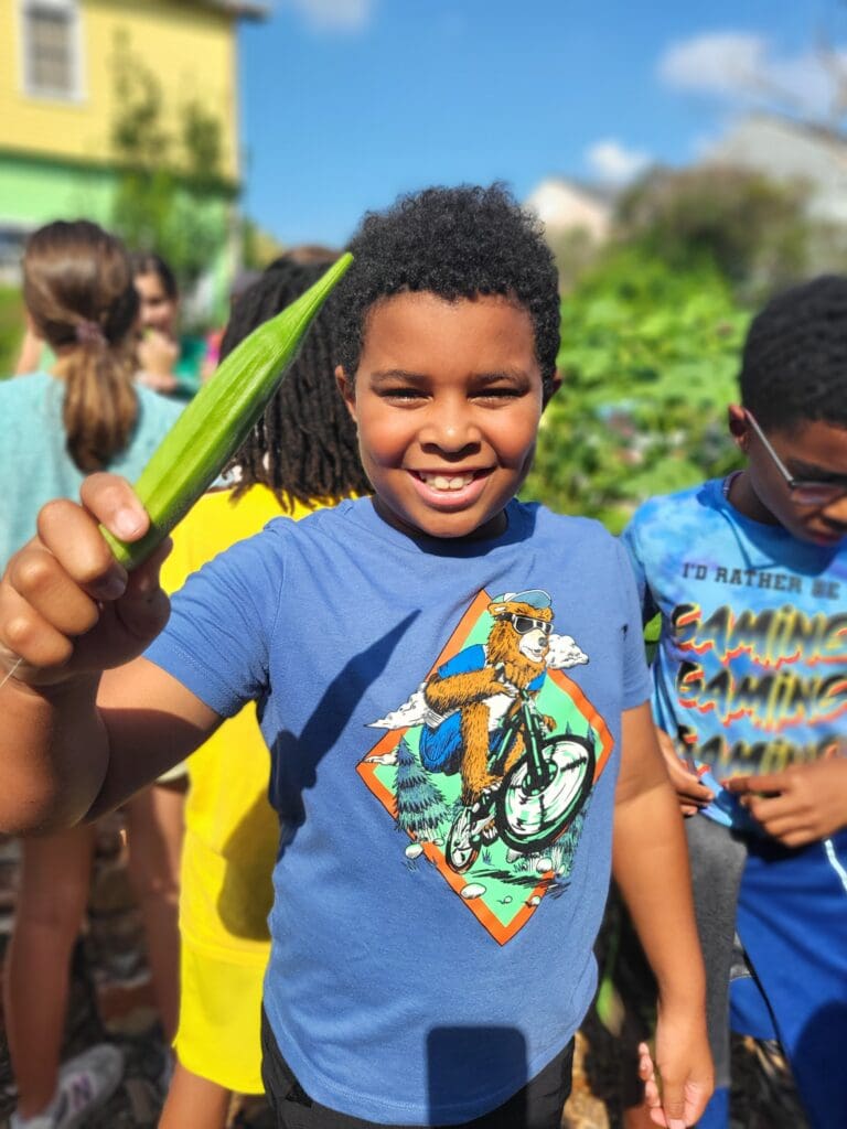 Nolavore camper holds up a piece of okra from the garden