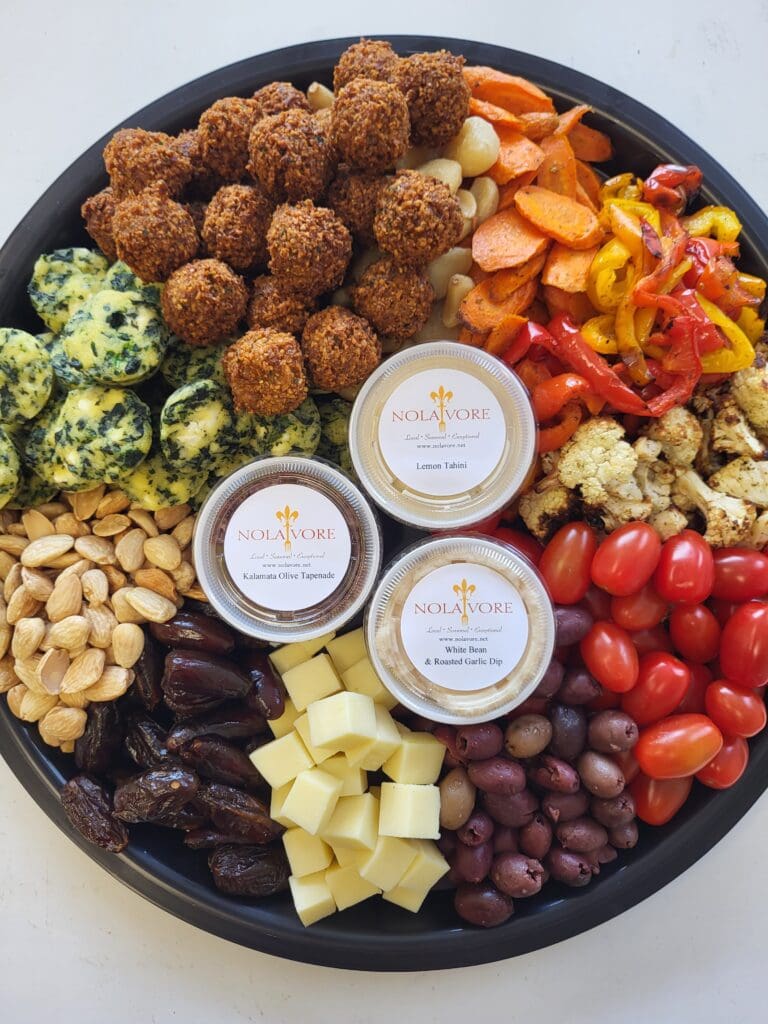 A tray of finger foods including cheese, olives, dates, tomatoes, roasted peppers, falafel, and almonds