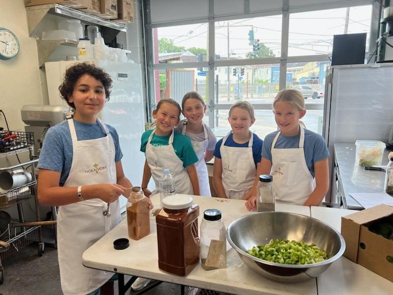 A group of children in a cooking class behind a table with a bowl of pepper chopped bell peppers
