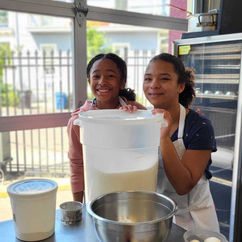 Two girls smiling at the camera in the kitchen while baking.